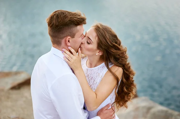 Bride and groom sitting on the beach and kissing — Stock Photo, Image