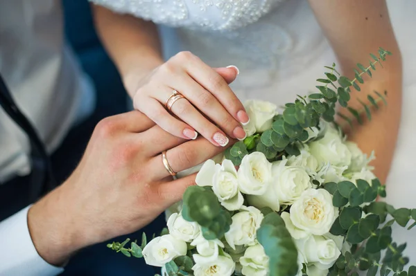 Руки жениха и невесты с кольцами на свадебном букете — стоковое фото