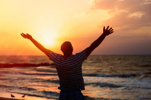 Ellerini gökyüzüne gün batımında sahilde yükselterek bir adam silüeti Stok Resim