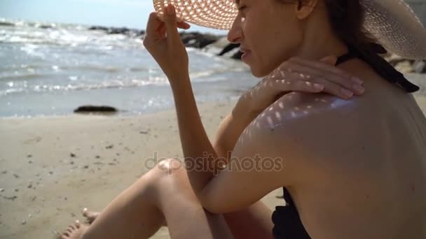 Junge Frau sitzt am Strand und reibt sich die Schultern — Stockvideo