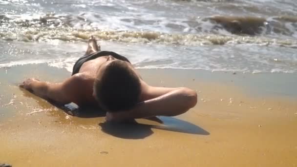 Jeune homme se trouve sur une plage de sable fin au bord de la mer — Video