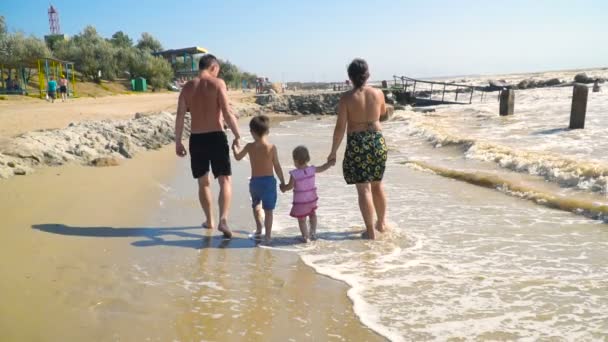 Junge Familie mit Kindern spaziert am Sandstrand entlang und hält Händchen — Stockvideo