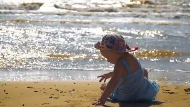 Mała dziewczynka siedzi na piaszczystej plaży i jest malarstwo na piasku — Wideo stockowe