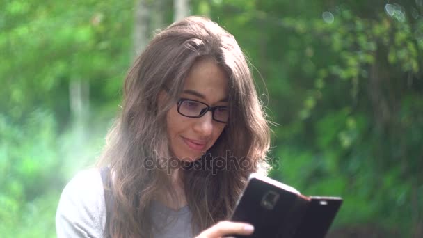 Красива молода жінка зі смартфоном в літньому парку — стокове відео