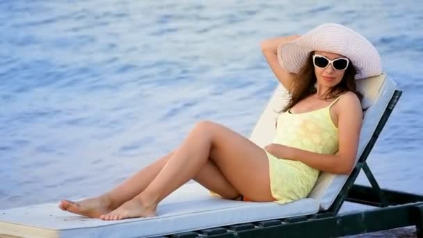 Bella giovane donna in occhiali prendere il sole sulla spiaggia contro il mare — Video Stock