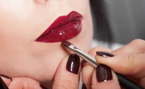 Maquillaje artista pinta una chica labios con lápiz labial rojo — Foto de Stock