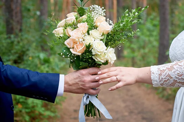 Noivo dá à noiva um buquê de casamento para um passeio no parque — Fotografia de Stock