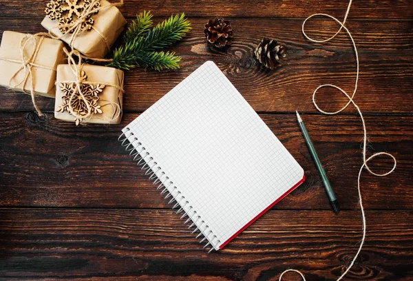 Christmas sammansättning uppsättning kraft presentaskar och träleksaker, majs och noterar med penna på trä bakgrund — Stockfoto