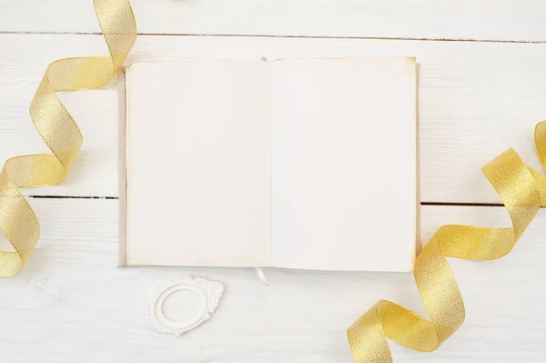 Mock-up open notebook on white wooden background with gold ribbon