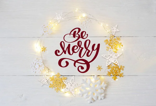 Text Be Merry in a Christmas con ghirlande e fiocchi di neve su fondo ligneo. Flat lay, vista dall'alto foto mockup — Foto Stock