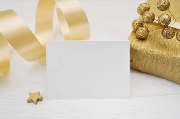 Mockup Christmas greeting card with gold gift ribbon, flatlay on a white wooden background, with place for your text — Stock Photo, Image