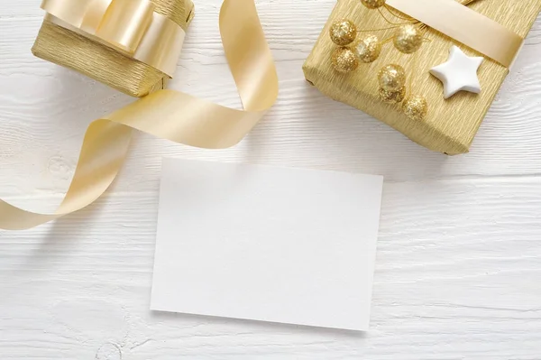 Mockup Noel tebrik kartı ile altın hediye kurdele, metniniz için yer ile beyaz ahşap zemin üzerinde flatlay — Stok fotoğraf
