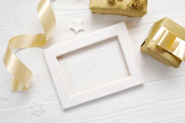 Mockup Christmas cadre blanc avec un ruban doré et un cadeau, flatlay sur un fond en bois blanc, avec place pour votre texte — Photo