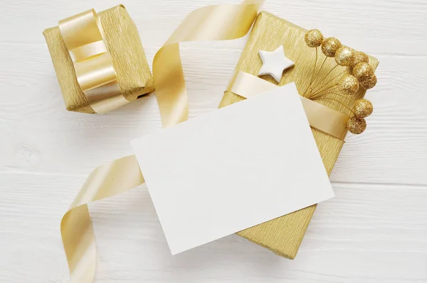 Mockup jul gratulationskort med guld gåva band, flatlay på en vit trä bakgrund, med plats för text — Stockfoto