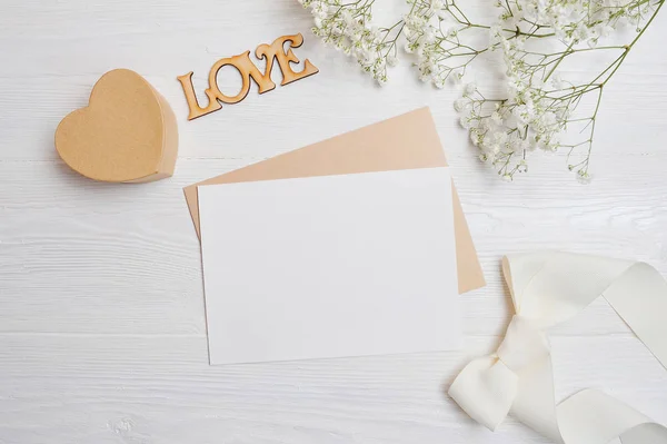 Mock up carta con una caja de amor en forma de corazón se encuentra en una mesa blanca de madera con flores de gypsophila, una tarjeta de felicitación para el día de San Valentín con un lugar para su texto. Puesta plana, vista superior foto — Foto de Stock