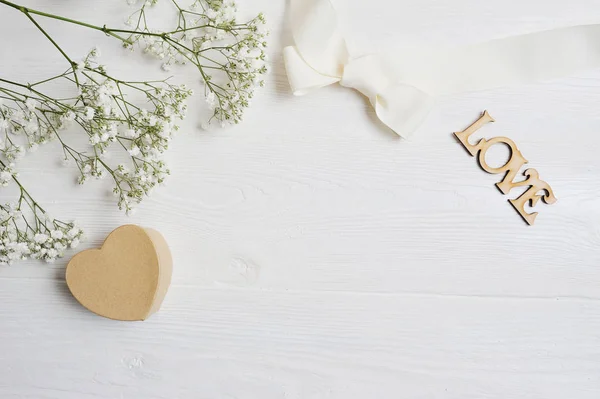 Mockup bloemen samenstelling van een witte cadeau gypsophila met een hart en een inscriptie hou op witte houten achtergrond. De dag van Valentijnskaarten. Plat lag, top uitzicht met een plek voor uw tekst — Stockfoto