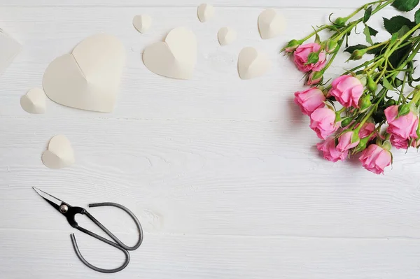 Mockup corazones de origami blanco hecho de papel con rosas rosadas y tijeras, tarjeta para el Día de San Valentín. Plano laico, vista superior con un lugar para su texto —  Fotos de Stock