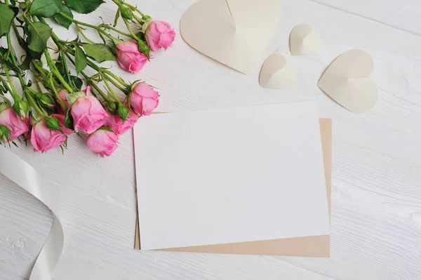 Mockup lettre blanc origami coeurs en papier avec des roses roses, carte pour la Saint-Valentin. Pose plate, vue du dessus avec une place pour votre texte — Photo