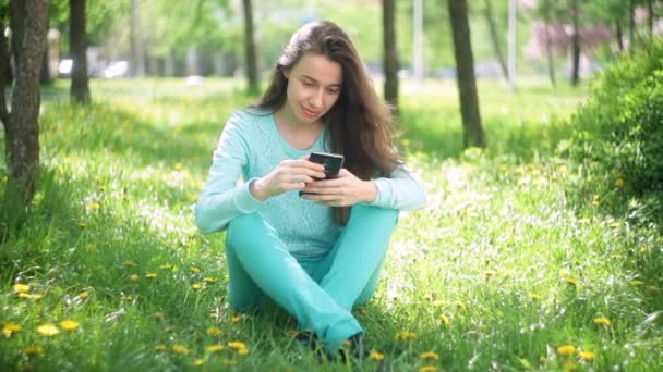 Lachende mooie toeristische jongedame ontspannen in het voorjaar bloeiende park met telefoon — Stockvideo