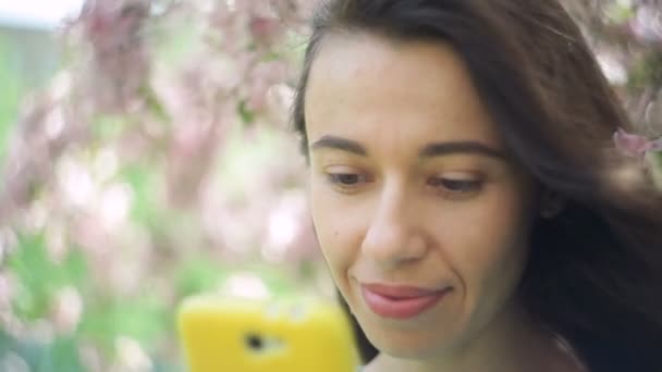 Lachende mooie toeristische jongedame ontspannen in het voorjaar bloeiende park met telefoon — Stockvideo