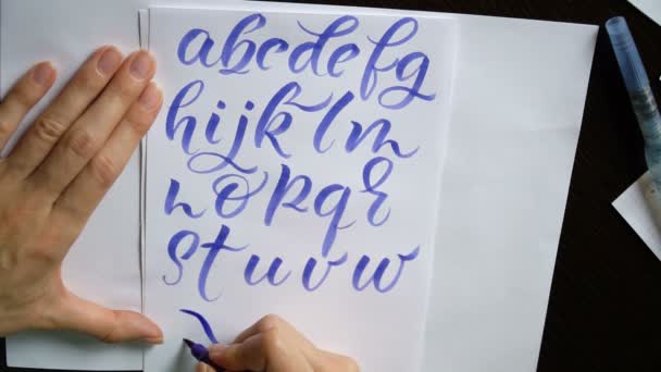 Motion video female hand writes a calligraphic alphabet in office — Stock video