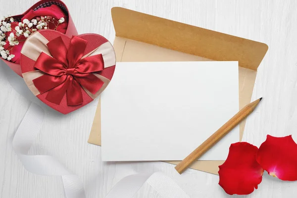 Mockup kraft envelope and a letter with a heart-shaped gift with a red bow and rose petals, greeting card for Valentines Day with place for your text. Flat lay, top view photo mock up — Stock Photo, Image