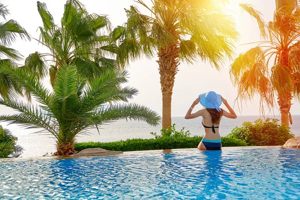 Jeune femme en chapeau d'été assis au bord de la piscine en voyage en mer — Photo