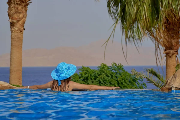 Young woman in summer hat in the pool on a trip to the sea and looks at the sunset in Egypt — Stock Photo, Image