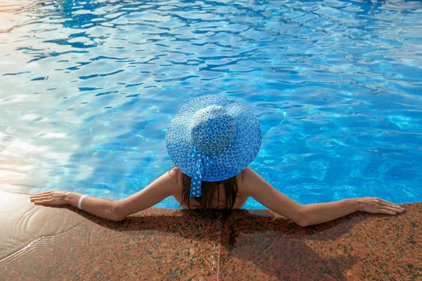 Beautiful woman in a hat sitting on the edge of the swimming pool summer in outdoors — Stock Photo, Image