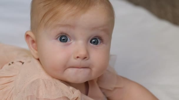 Bellissimo bambino sorridente: Una bellissima bambina giace su una coperta bianca e sorride alla telecamera con un bel occhione. chiudere 4k video — Video Stock