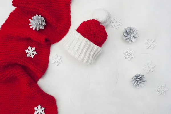Maqueta navideña con bufanda y sombrero rojo de Santa Claus sobre fondo de madera con conos, copos de nieve y lugar para tu texto. Tarjeta de felicitación de vacaciones —  Fotos de Stock