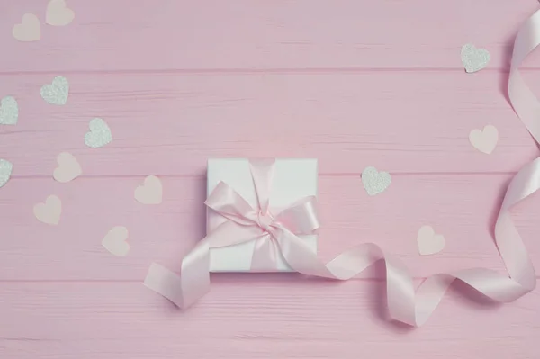 Caja de regalo con cinta y confeti en forma de corazón sobre fondo de madera rosa con lugar para su texto. Finge el día de San Valentín, el día de las madres o el cumpleaños. Vista superior, plano — Foto de Stock