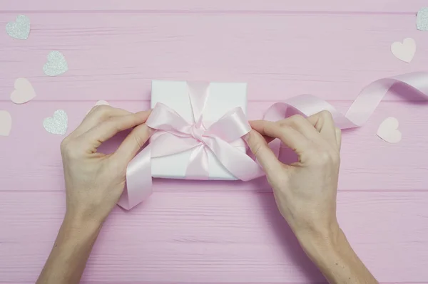 Valentine love concept of beautiful womans hands hold gift box rzemieślnicze papieru i serca konfetti na różowym tle. widok z góry płaski leżał z miejscem na tekst — Zdjęcie stockowe