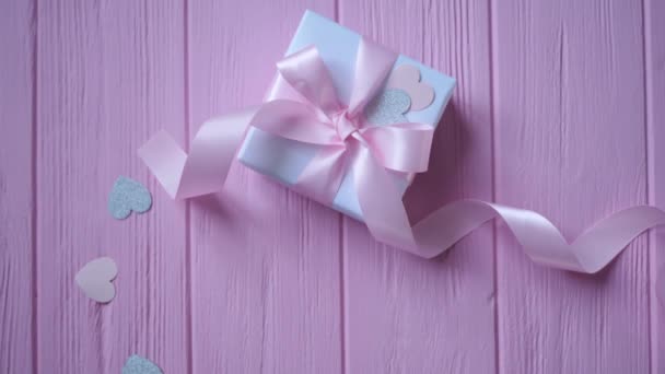 Caja de regalo con cinta y confeti en forma de corazón sobre fondo de madera rosa con lugar para su texto. Movimiento de vídeo en el Día de San Valentín, día de las madres o cumpleaños. Vista superior HD — Vídeos de Stock