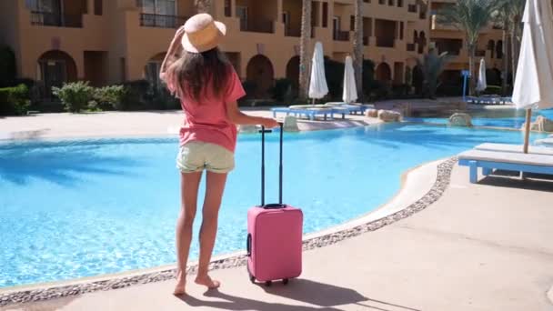 Молода жінка з рожевою чемоданчиною залишається біля басейну в готелі. Концепція туристичних канікул. Hd video in Prores 1920x1080 — стокове відео