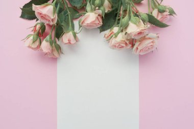 wedding or birthday mock up scene. Blank open sheet of paper with place for text for greeting card. Bouquet of pink roses on pink background. Flat lay, top view