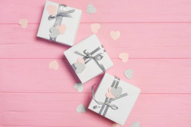 Gift white boxes with silver satin ribbon and confetti in form of heart on pink background love. Mock up on Womens Day, Valentines day, happy birthday