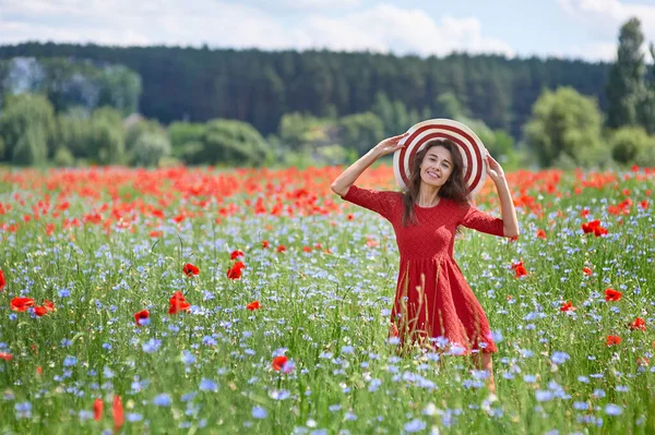 Kırmızı elbise ve güzel ot çiçekli haşhaş alanında büyük bir kırmızı çizgili şapka dreamy kadın. Vintage zarif romantik bir görünüm. güzel yaz kavramı — Stok fotoğraf