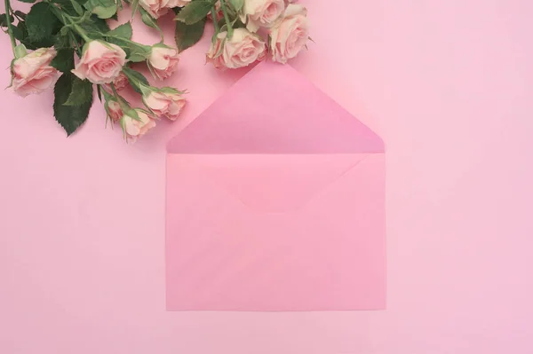 wedding or birthday mock up scene. Blank open envelope with place for text for spring greeting card. Bouquet of pink roses on pink background. Flat lay, top view