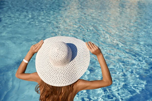 Rear view of woman in white hat sitting near pool on a sunny day. Sea travel concept with place for your text — Stok fotoğraf