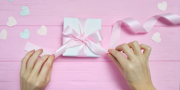 Valentine kärlek koncept vackra kvinnor händer hålla presentförpackning hantverk papper och hjärta konfetti på rosa bakgrund. ovanifrån platt låg med plats för text — Stockfoto