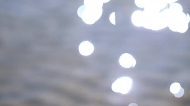 Azul e espumante fundo de luz Bokeh no mar. refletindo na luz solar com um bokeh. Tiro desfocado de uma superfície de água com um belo bokeh de clarões de sol que se refletem do mar — Vídeo de Stock