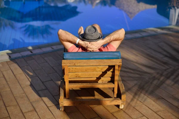 Relájese en la piscina de verano. Joven y exitoso hombre acostado en una tumbona y levantando los brazos en el hotel cerca de la piscina sudorosa. Concepto tiempo para viajar — Foto de Stock