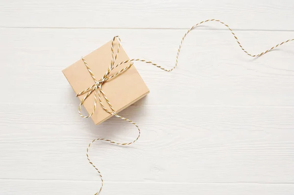 Caja de regalo en papel kraft con un arco de cuerda está en una mesa de madera blanca, con lugar para su texto — Foto de Stock