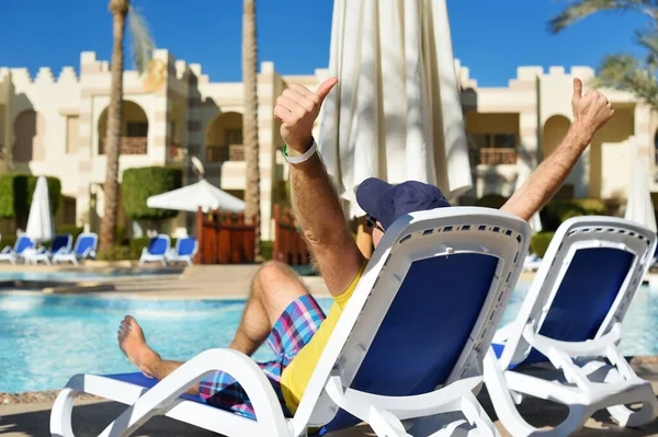 Entspannen Sie sich im Sommerpool. junger und erfolgreicher Mann, der auf einer Sonnenliege liegt und die Arme am Hotel in der Nähe des Schwimmbeckens hebt. Zeit zum Reisen — Stockfoto