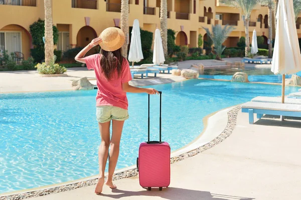 Voyage, vacances d'été et concept de vacances - Belle femme marchant près de la piscine de l'hôtel avec valise rose — Photo