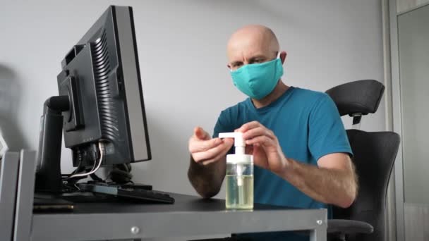 보호용 마스크를 쓰고 집에서 일하는 남자가 질식사용 겔로 손을 닦고 있습니다. 코로나 바이러스 격리 조치 집에서 일하는 모습 — 비디오