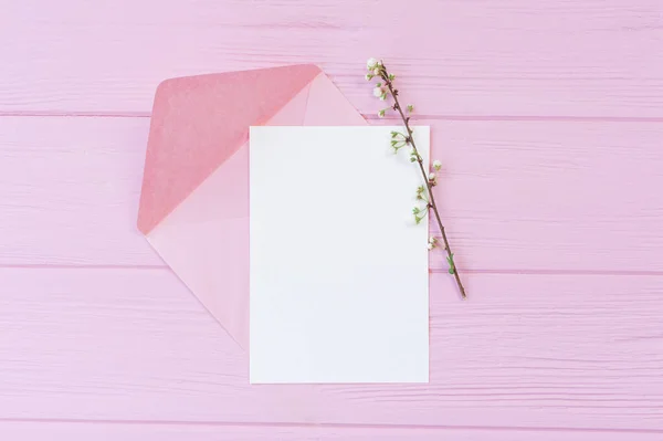 Tak van witte kersenbloemen op roze houten achtergrond met vel mockup papier, en enveloppe met plaats voor uw tekst. Voor wenskaart, banner, poster. Voorjaarsvakantie concept — Stockfoto