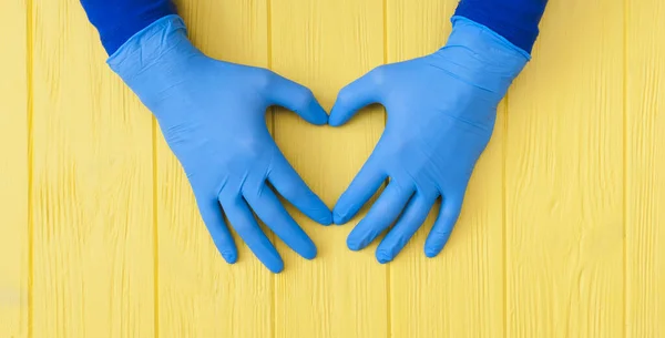 Rękawice Blue Nitrile. Ręce medyka w niebieskich rękawiczkach lateksowych na żółtym drewnianym stole z transparentem — Zdjęcie stockowe