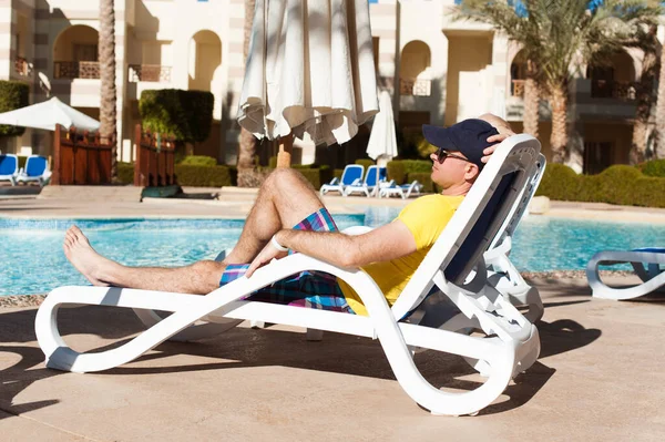 Homme jeune et prospère allongé sur une chaise longue à l'hôtel près de la piscine. Détendez-vous dans la piscine d'été. Concept temps de voyager été — Photo